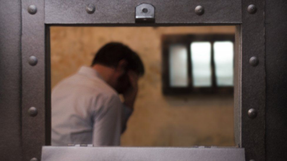 A prisoner in a cell with his head in his hands
