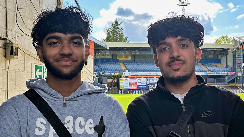 Umor Uddin (left) and Atif Khan (right) stood next to each other smiling with the Luton Town football ground in the background