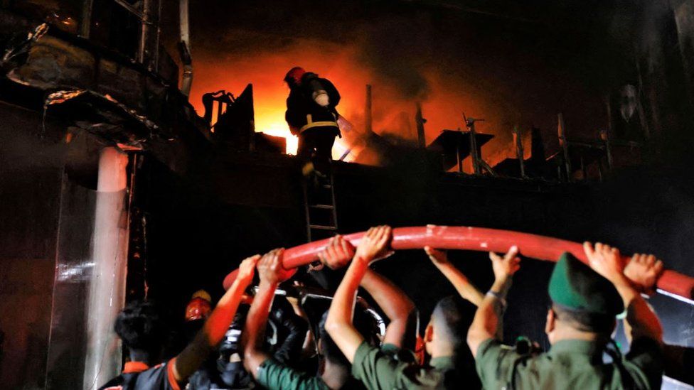 Volunteers carry a water pipe as firefighters spray water to douse the fire that broke out in a multi-storey building in Dhaka