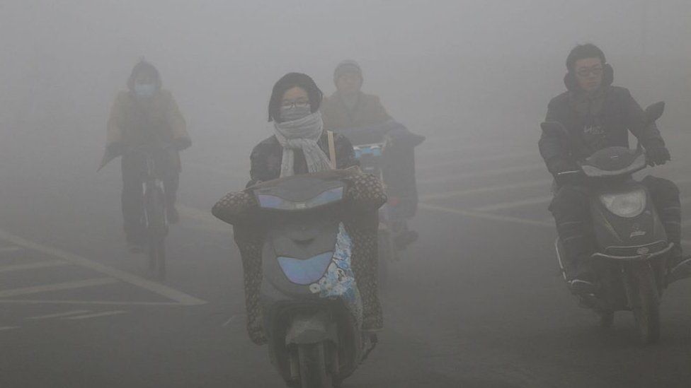 Cyclists wearing masks ride along a road in heavy smog on December 23, 2015 in Zhengzhou, China.