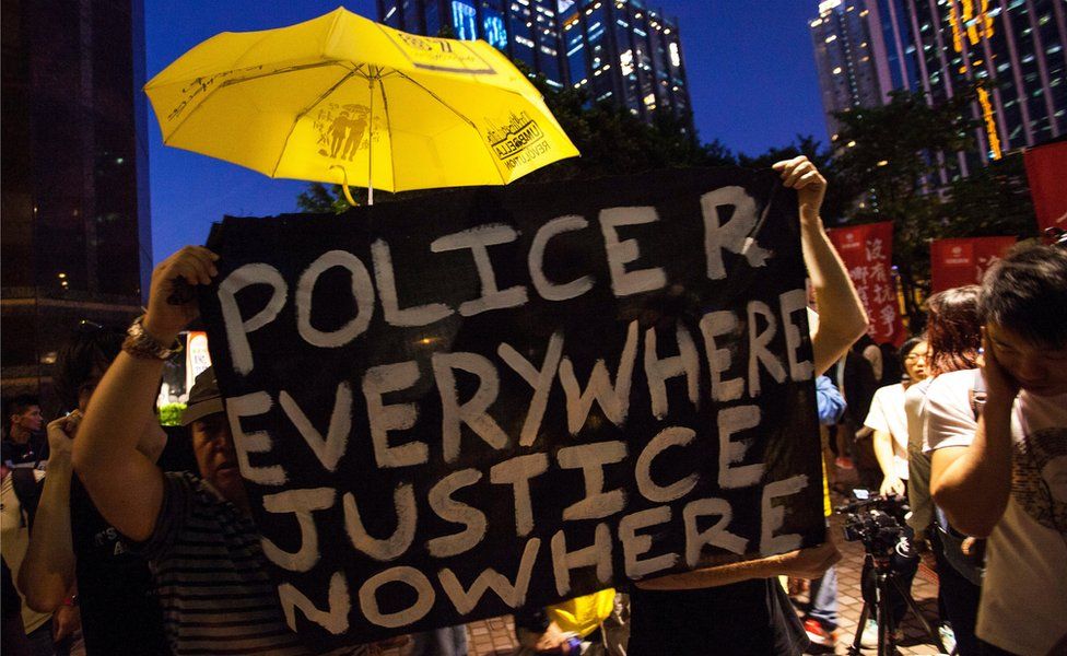 Pro-democracy protesters hold a yellow umbrella - a symbol of the territory's pro-democracy movement - and a banner reading 'police r everywhere justice nowhere", near the venue of where Zhang Dejiang gave a keynote speech on 18 May