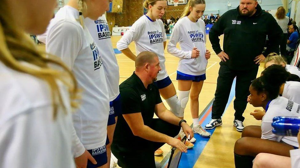 Coach Nick Drane crouching courtside, instructing his team