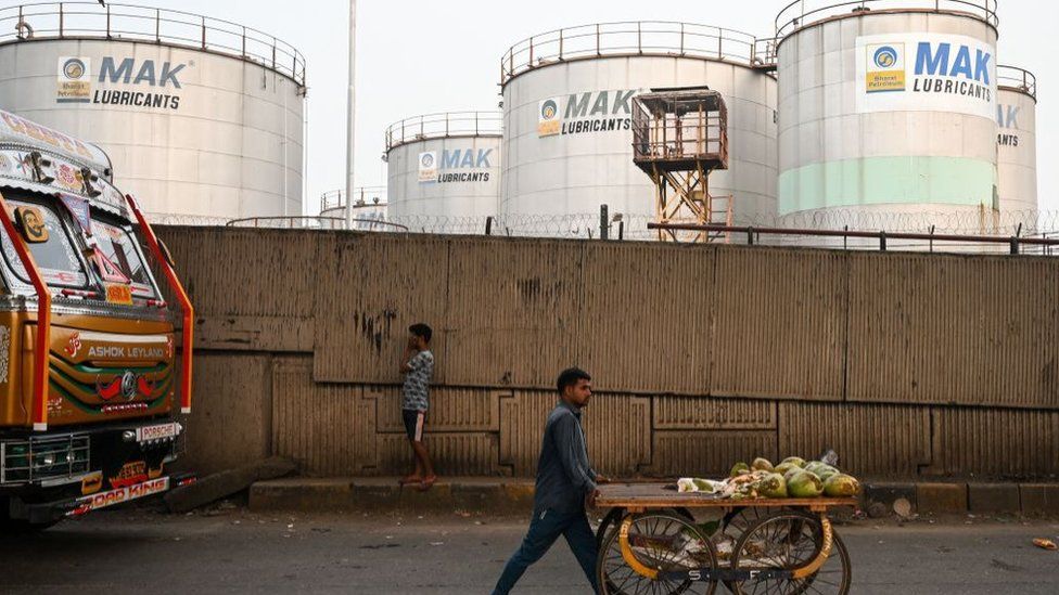 A man pushes his cart as he walks past Bharat Petroleum's storage tankers in Mumbai on December 8, 2022.