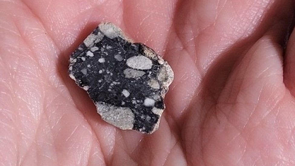 Рука держит кусок лунного камня, найденный в Сахаре