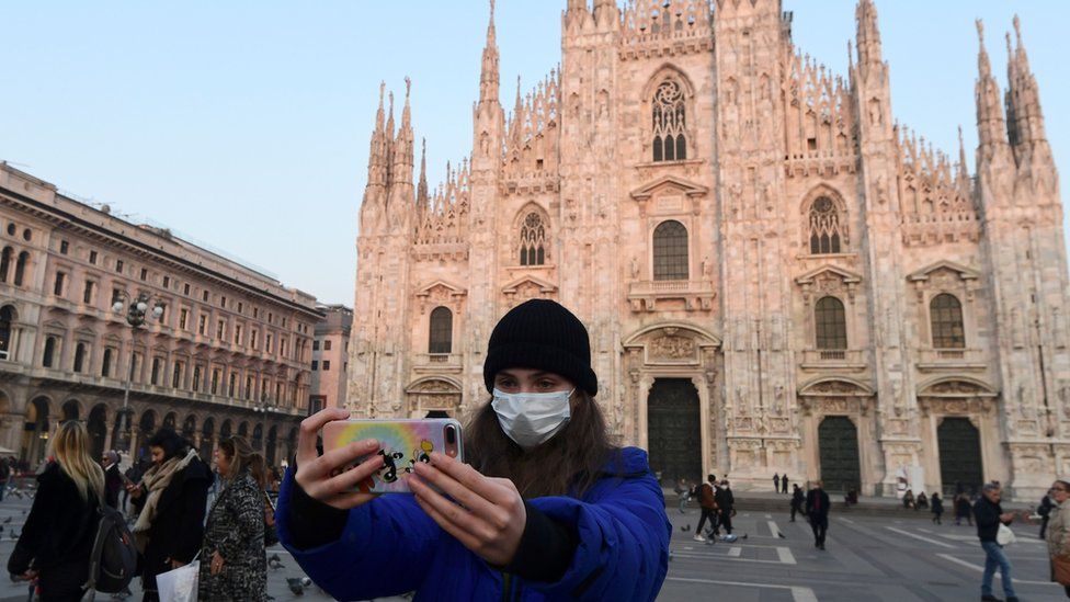 A tourist in a protective mask takes a selfie in the Piazza del Duomo, Milan
