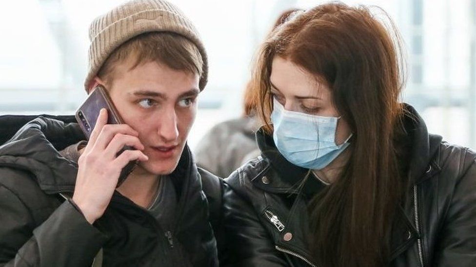A young woman wearing a face mask looks at her unmasked partner at a train station in the Russian city of Sochi