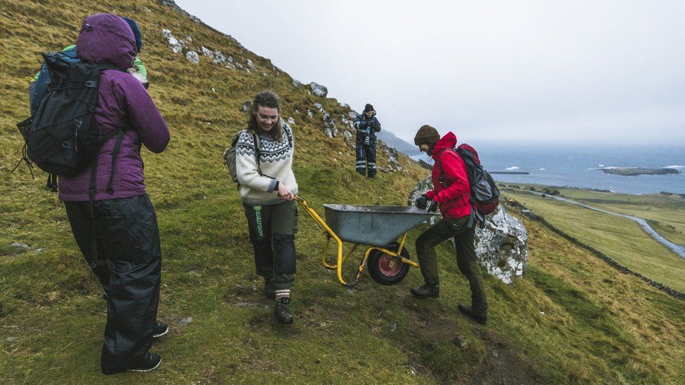 Brown Group members help each other to push a wheelbarrow in the hills in Kirkjubøur