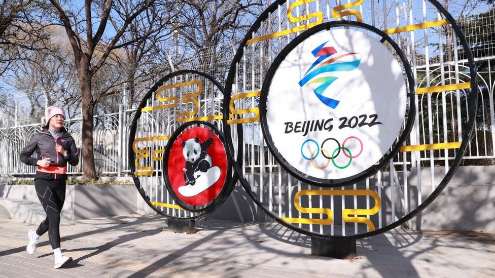 Женщина бежит перед вывеской Игр в Пекине