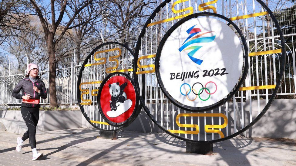 Pekin'de Kış Olimpiyatları süslemelerinin önünde koşuya çıkan bir kadın. BBC, 2021.