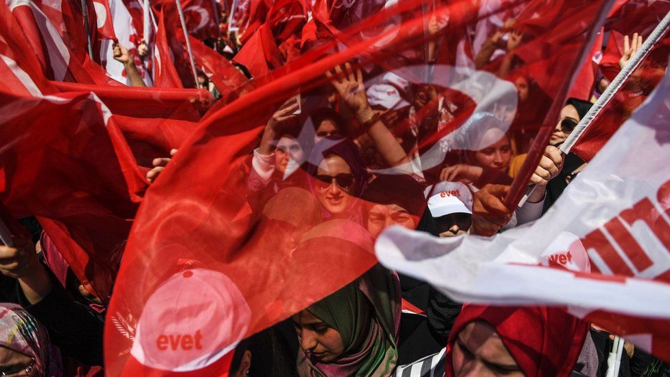 People cheer and wave flags as Turkey's President Recep Tayyip Erdogan delivers a speech on the eve of the constitutional referendum in Istanbul, 15 April 2017