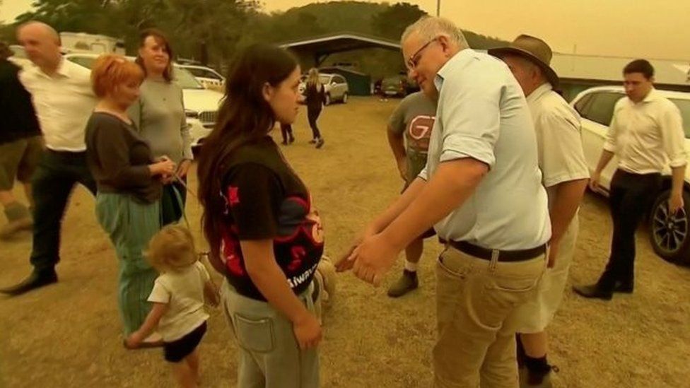 Scott Morrison moves to lift the hand of a woman in Cobargo, New South Wales