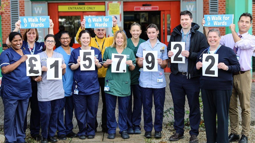 Hospital staff outside the entrance each holding a number showing the amount raised.
