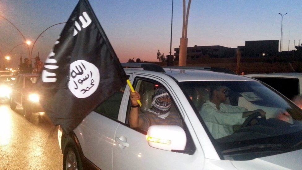 IS fighter waves a flag of the group in the city of Mosul, Iraq on 23 June