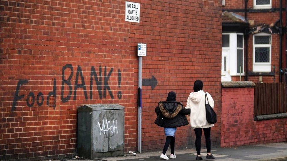 Woman and a child walking past a wall with 'food bank' painted on