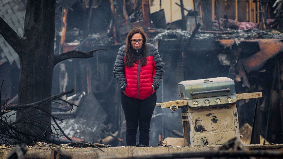 A woman stands in front of the remains of her cousin's house in Louisville