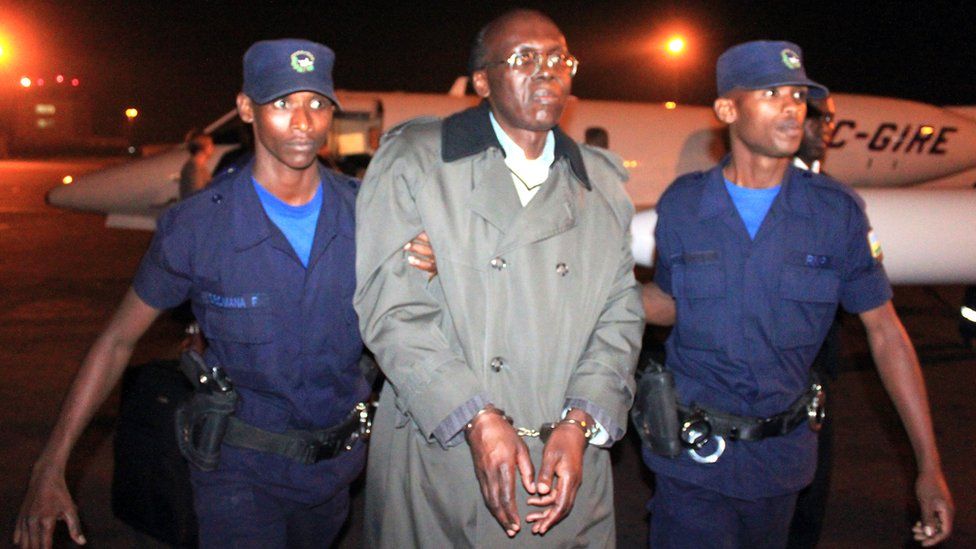 Leon Mugesera (C) is escorted handcuffed by policemen to a police vehicle on the tarmac as he arrives at Kigali International Airport late on January 24, 2012