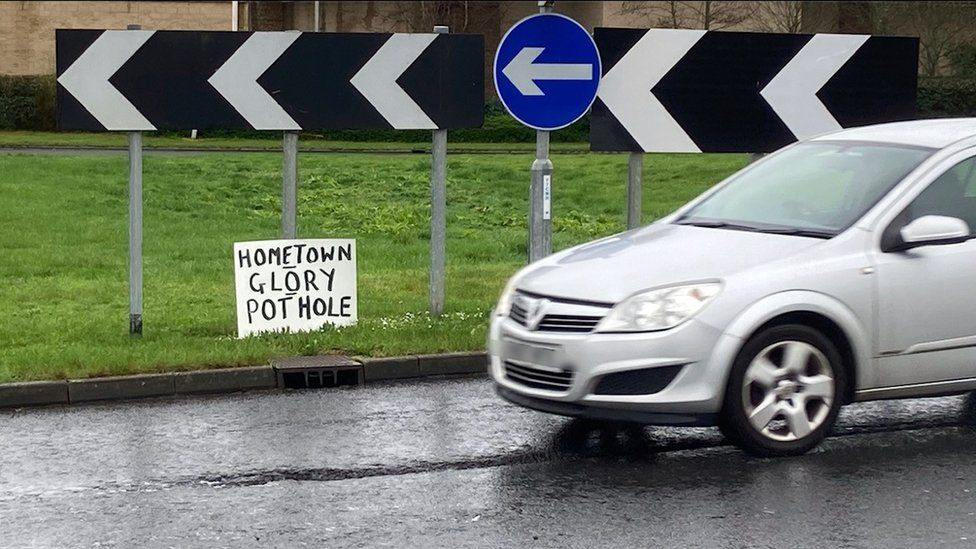 A small sign fixed to a roundabout direction sign