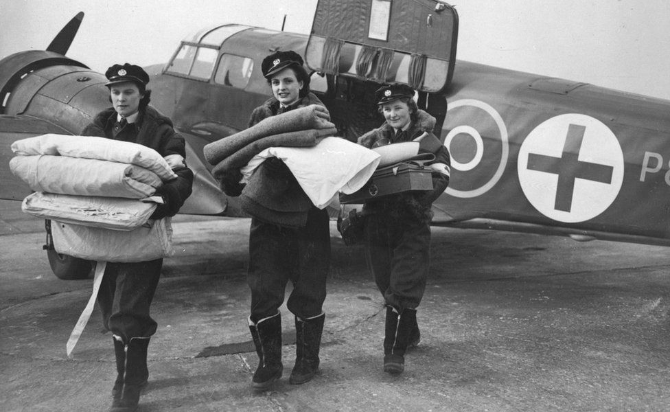 Black and white image of three Flying Nightingales carrying blankets away from RAF plane