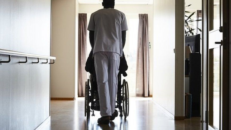 Care worker pushing a wheelchair down a corridor