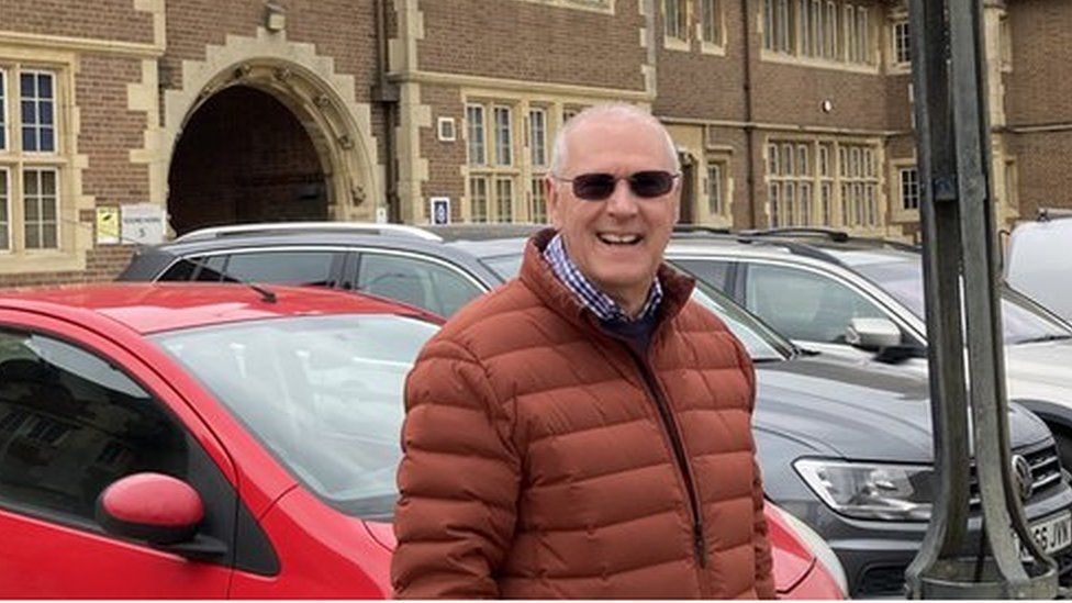 Martin Johns, wearing a brown coat, in front of the former police station. The 1930s building is red brick.