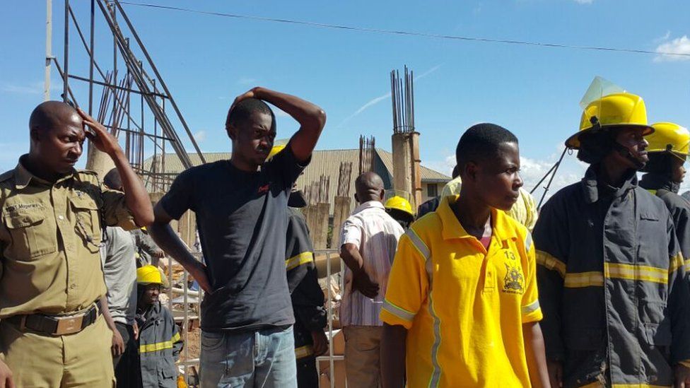emergency workers and site workers look on at the scene of the collapse