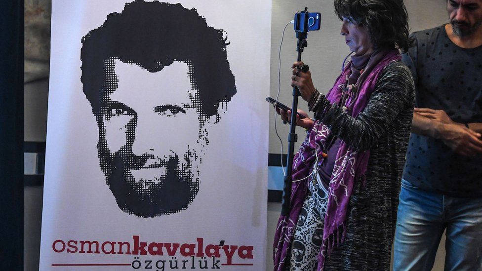 A journalist stands in front of a poster featuring jailed businessman and philanthropist Osman Kavala in October 2018