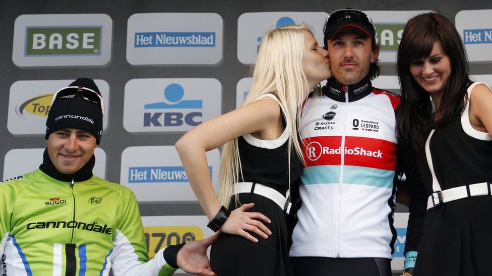 Peter Sagan pinching a podium girl's bottom on the winner's podium, with Fabio Cancellara and two podium girls in the picture