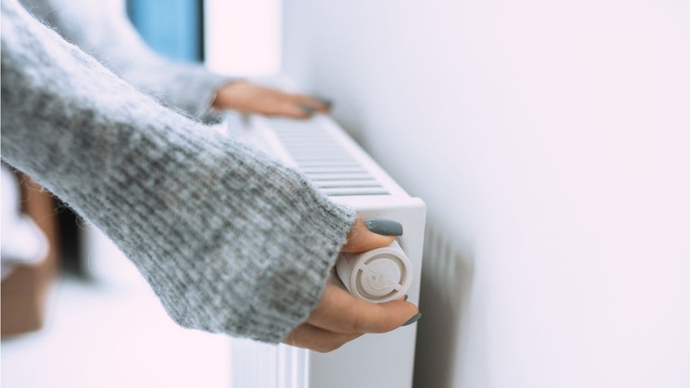 Woman wearing grey sweater sets radiator thermostat