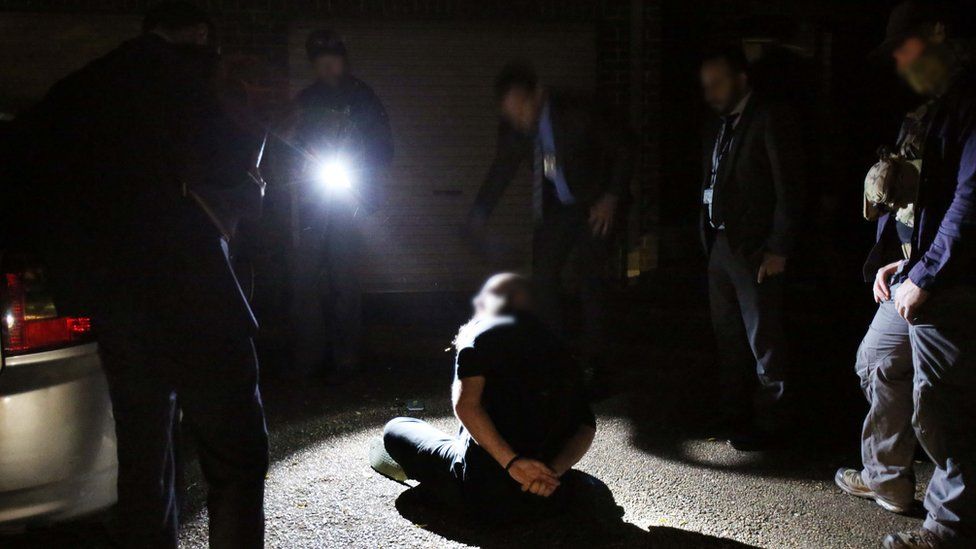 A young man is handcuffed as officers execute warrants at a home on Booth Street in Marsfield, Sydney