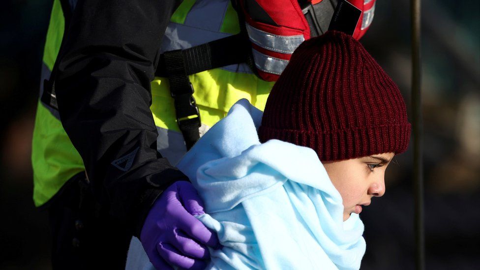 A migrant child is escorted by Border Force staff into Dover harbour after crossing the channel last week.