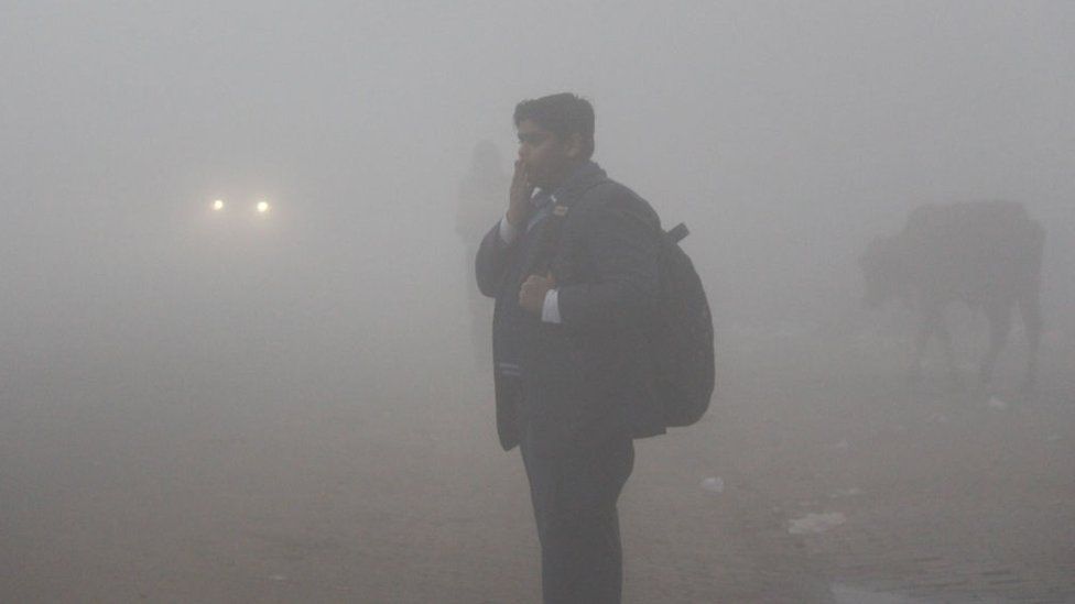 Ученики идут в школу в теплой одежде среди густого тумана холодным зимним утром 30 декабря 2019 года в Гуруграме, Индия.