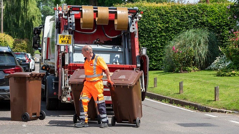 A council worker carrying bins near a lorry