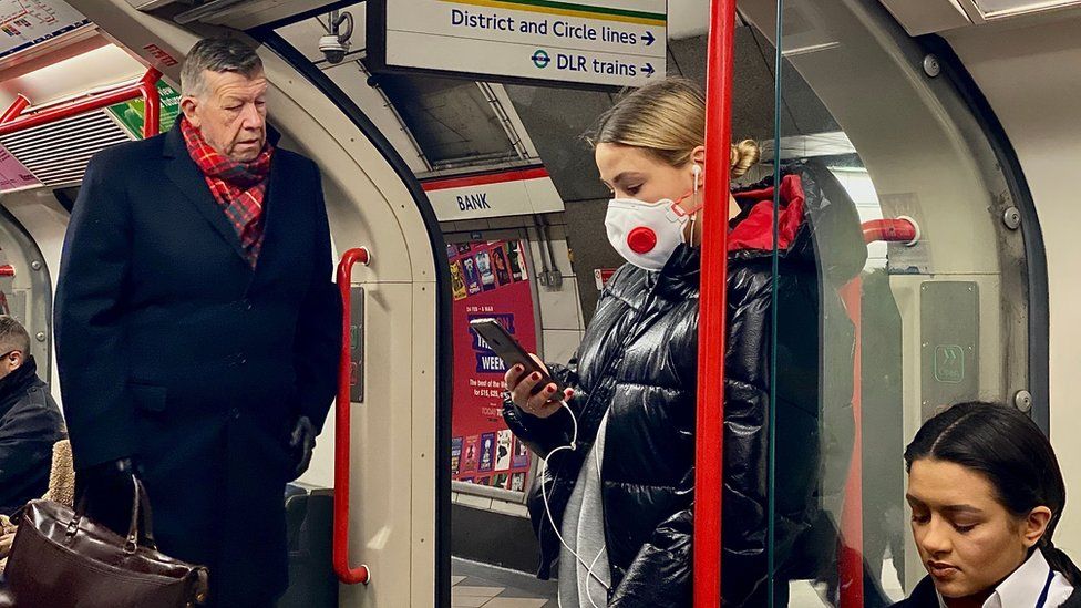 Travellers on the London Underground, one wearing a face mask