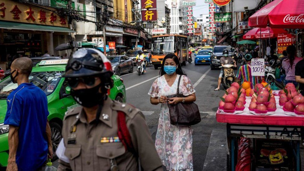 People wearing face masks walk past fruits stalls in Bangkok's Chinatown on May 1, 2021