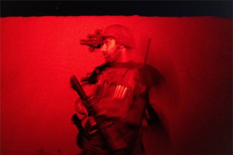 Сотрудник афганского спецназа наблюдает за тем, как другие обыскивают дом во время боевой операции против талибов в провинции Кандагар, Афганистан, 12 июля 2021 г.