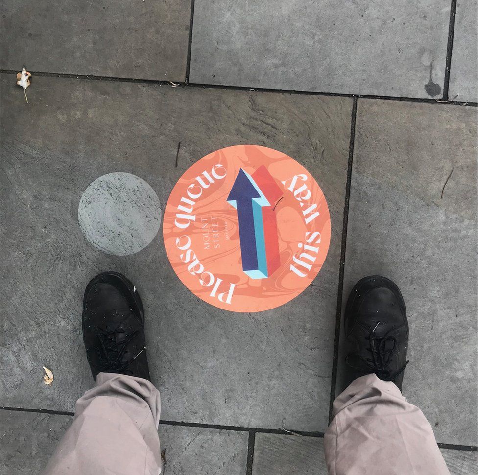 A sign on the ground pointing the way for people to queue