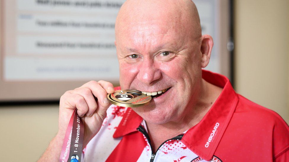 Neil Jones, 59, from Stoke-on-Trent, bites his bronze medal he won as part of the England B1 team which he captained at the European Blackball Championships in Malta in November.