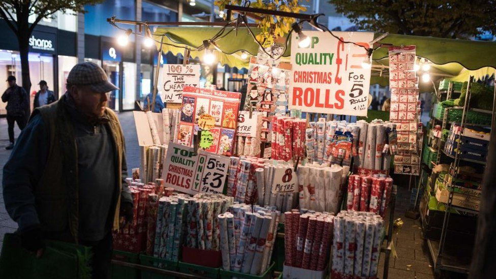 A man in a flat cap stands by a wrapping paper stall