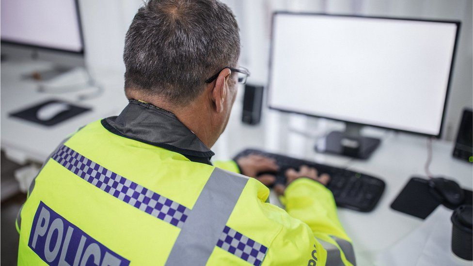 British police officer writing report on computer at the office