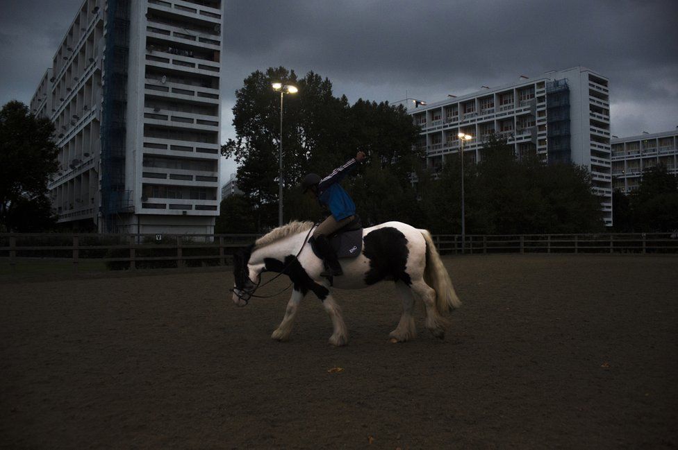 A boy rides a horse against a background of blocks of flats