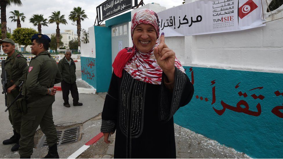 A Tunisian woman voter showcases her ink-stained index finger after voting in the first free municipal elections since the 2011 revolution
