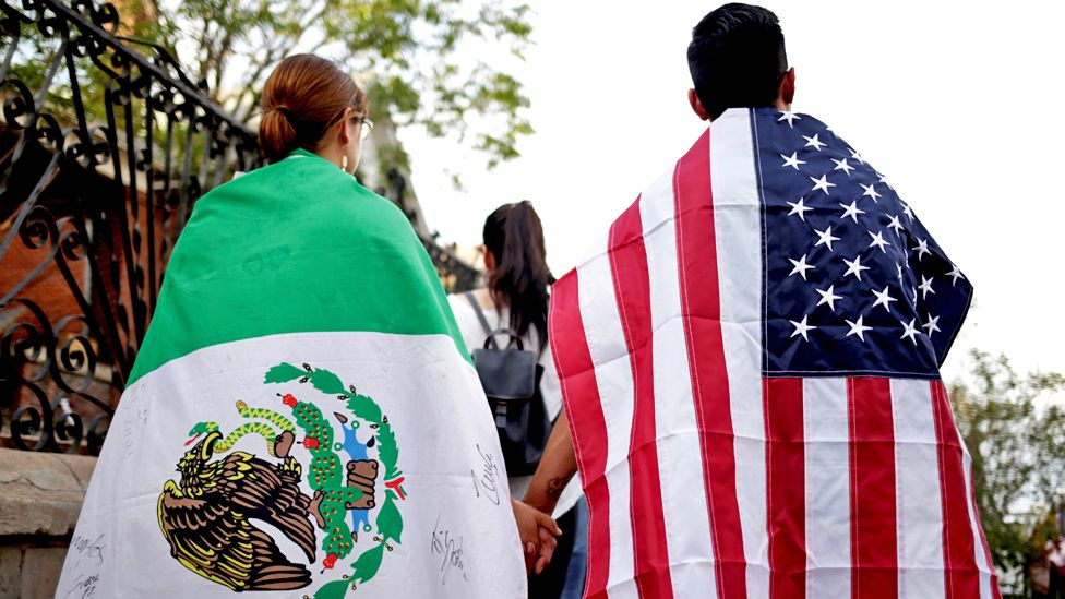 People draped in the Mexican flag and the US flag take part in a rally against hate a day after a mass shooting in El Paso