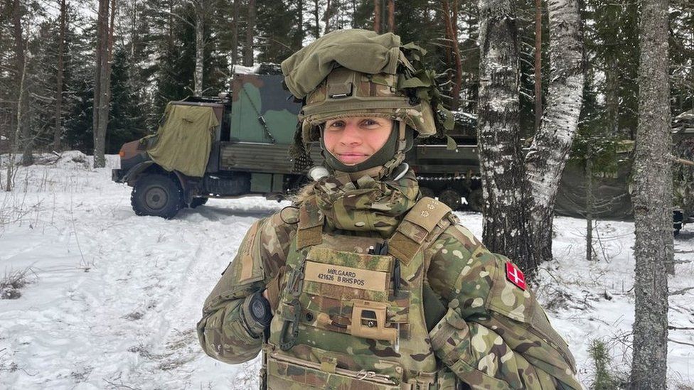 Female soldier from Denmark stands in front of snowy forest