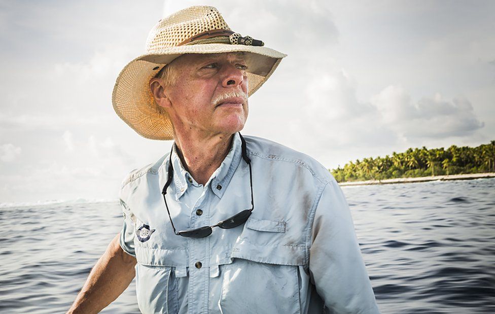 A picture of Ric Gillespie at sea in a straw hat and blue shirt