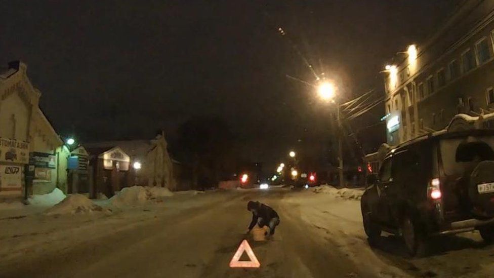 Still from a video showing Miss Bobrus filling a pothole at night