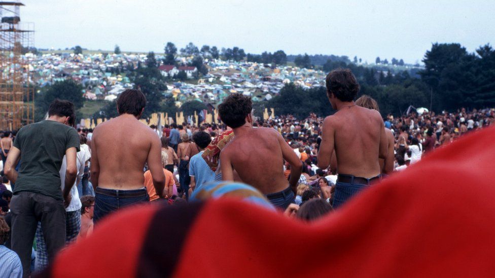 Three sunburned men stood up in front of a large crowd of people