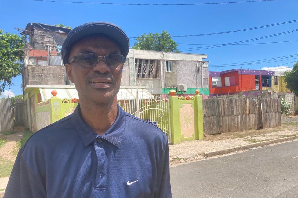 Dr Howard Harvey stands in front of a colourful lime green fence in Trench Town