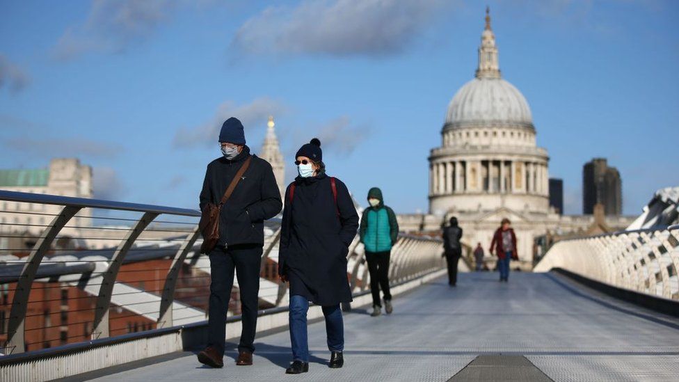 Pedestrians wearing masks cross Millennium Bridge with St Paul's Cathedral in the background