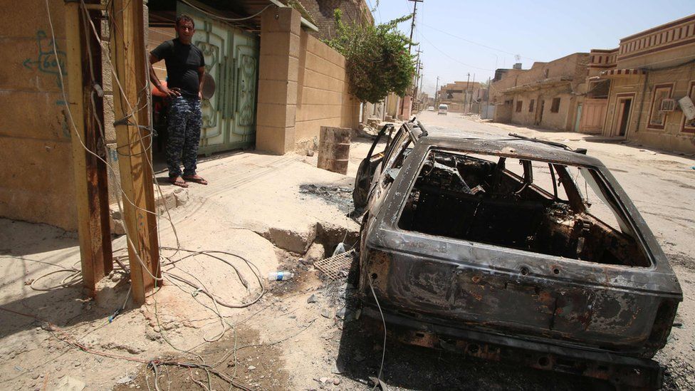 Member of Iraqi security forces stands near a burned-out car in Falluja (25 June 2016)