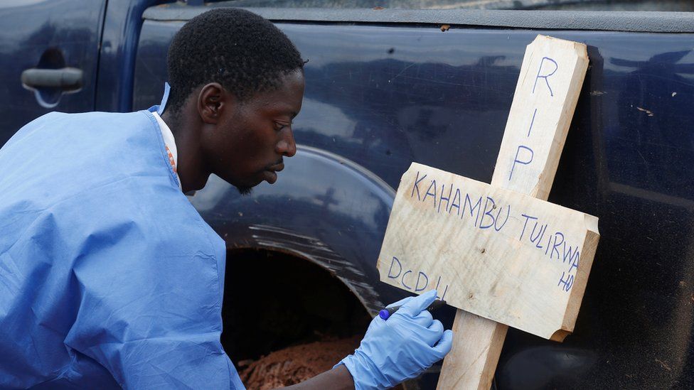 A health worker writes the name of an Ebola victim on a cross